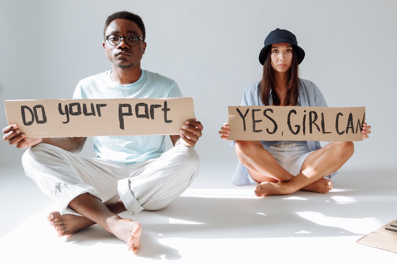 African American man and Asian woman sitting with cardboard signs promoting empowerment.